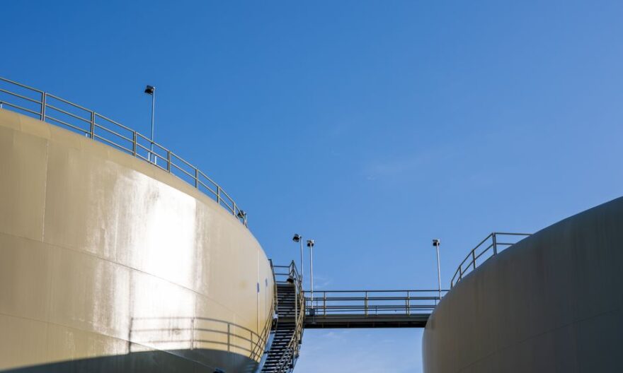Sunlit industrial silos connected by a staircase under a clear blue sky. - Photo by David Brown on Pexels