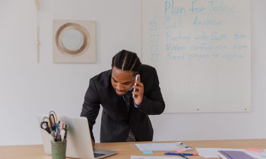 Businessman in an office making a call while working on a laptop with office supplies. - Photo by RDNE Stock project on Pexels