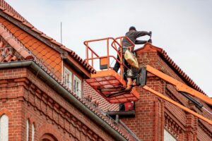 Roofer in a cherry picker conducting maintenance on a red brick building with a tiled roof. - Photo by Gundula Vogel on Pexels