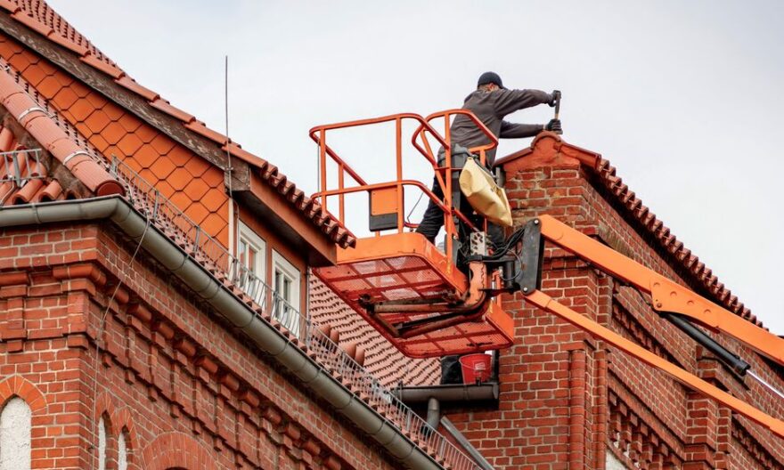 Roofer in a cherry picker conducting maintenance on a red brick building with a tiled roof. - Photo by Gundula Vogel on Pexels