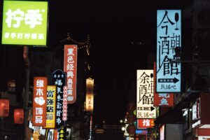 A bustling city street at night illuminated by colorful neon signs in various scripts. - Photo by YIMING TANG on Pexels