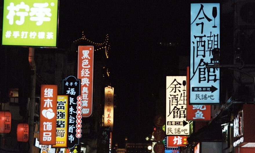 A bustling city street at night illuminated by colorful neon signs in various scripts. - Photo by YIMING TANG on Pexels